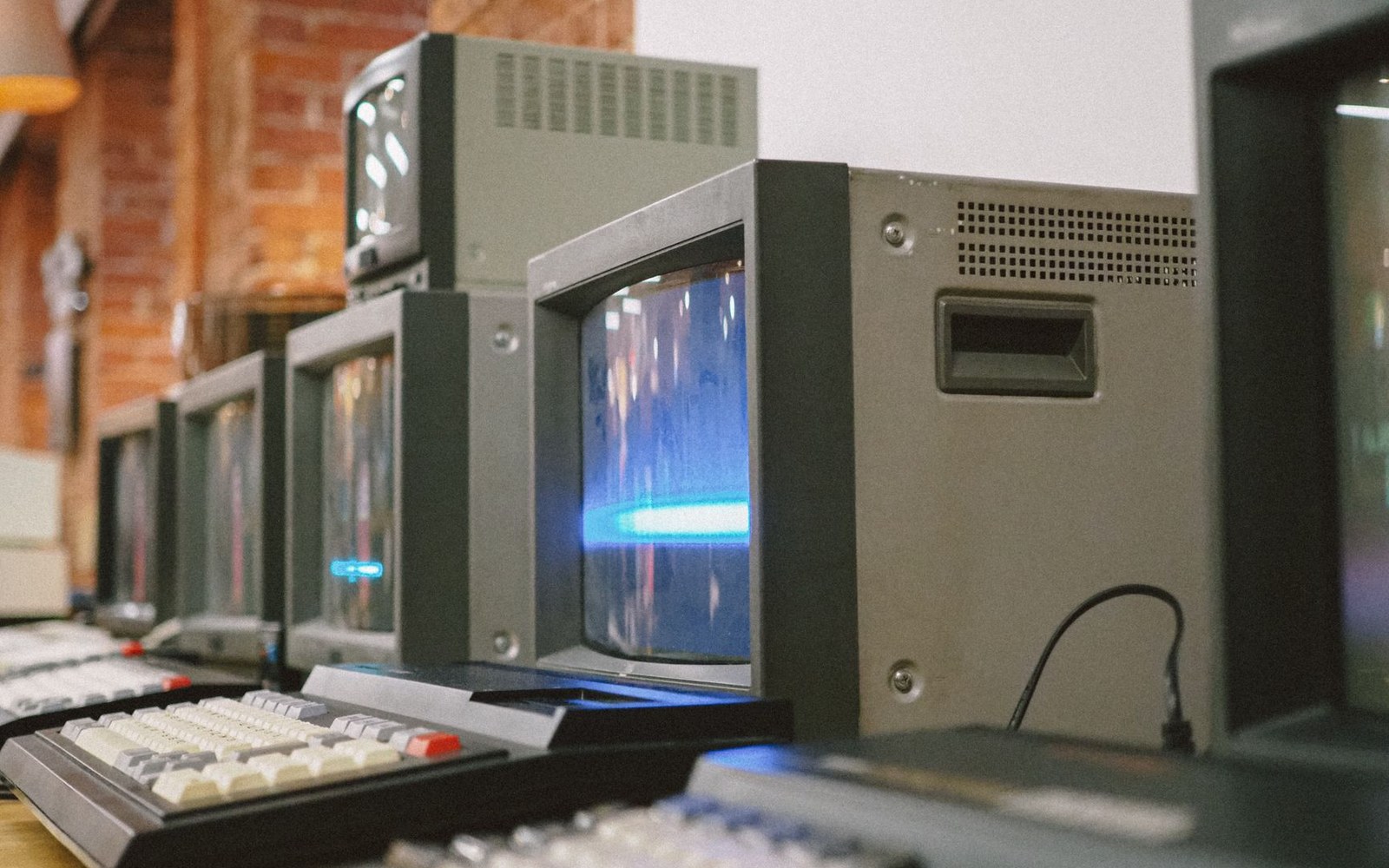 A row of CRT terminals in a dimly lit 1980s computer room, screens showing green-phosphor text, with a developer visible at the nearest station